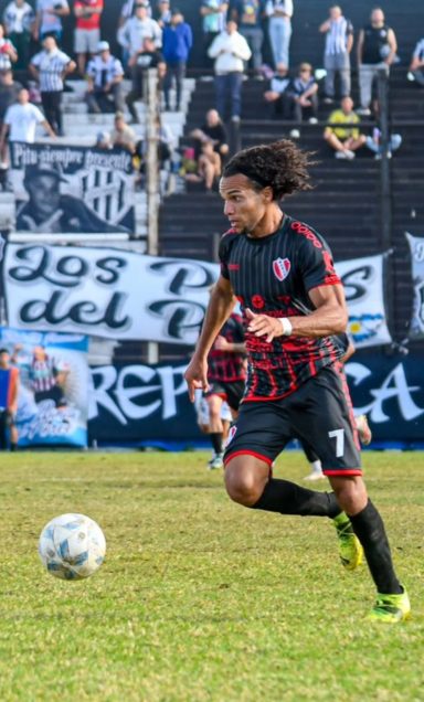Jugador de fútbol corre con el balón en un campo, mientras la afición anima.